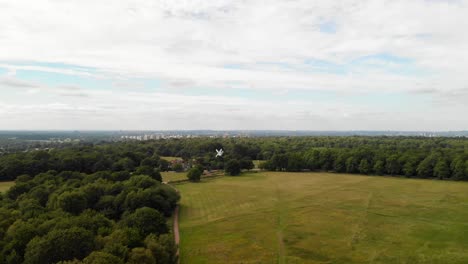 Aerial-view-of-Wimbledon-Common-with-a-view-of-London-city-and-a-small-windmill-in-the-center-of-the-frame,-establish-shot