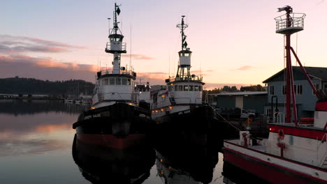 Drone-ascending-over-two-large-boats-docked-at-Coos-Bay-Wharf,-sunset