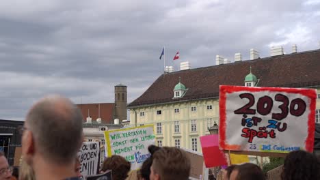 View-of-crowd-holding-up-signs-with-backdrop-of-Austrian-and-European-flag-during-fridays-for-future-climate-change-protests-SLOW-MOTION