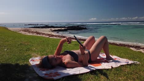 Eine-Aufnahme-Einer-Frau,-Die-Am-Strand-An-Einem-Wunderschönen-Ort-In-Mauritius-In-Einem-E-Book-Liest