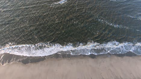 Aerial,-rising,-drone-shot-above-small-waves-hitting-a-beach,-at-the-North-sea,-on-Langeoog-island,-in-North-Germany