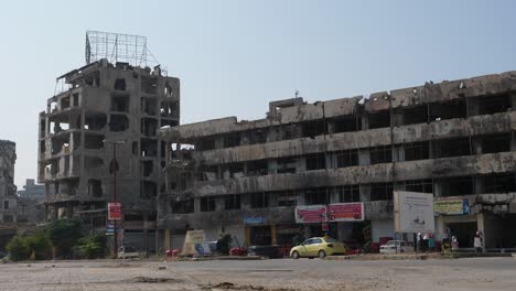 Stetige-Aufnahme-Aus-Niedrigem-Winkel,-Autos-Fahren-An-Einem-Riesigen-Verlassenen-Und-Zerstörten-Gebäude-In-Der-Stadt-Homs-Vorbei