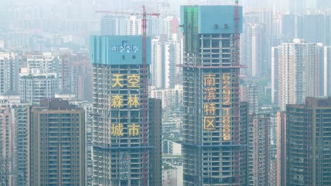 Twin-buildings-under-construction-with-red-cranes-with-concrete-retainers-and-showing-city-with-air-pollution-haze,-Locked-establishing-shot