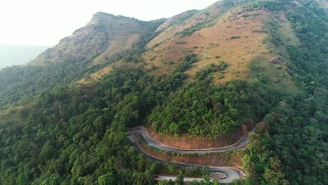 Winding-mountain-pass-road-between-trees,-aerial-push-out