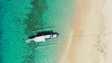 Indonesian-Coast-Showing-Beautiful-Crystal-Green-Waters-With-A-Boat-Suspending-At-The-Shoreline---Aerial-Shot