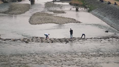 Drei-Männer-überqueren-Die-Trittsteine-Und-Spielen-Auf-Dem-Wasser-Am-Kamogawa-Fluss-In-Kyoto,-Japan