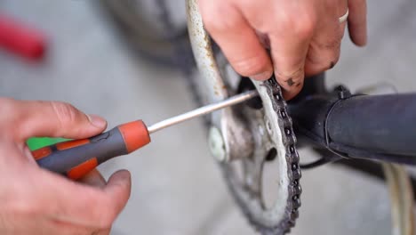 Caucasian-male-mechanic-fingers-tighten-screw-on-frame-of-bicycle-with-screwdriver,-above-close-up-static