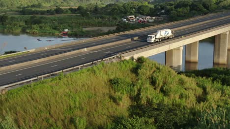 Rising-drone-shot-of-a-single-cement-truck-driving-over-the-Umzimkhulu-highway-bridge-in-Port-Shepstone,-South-Africa
