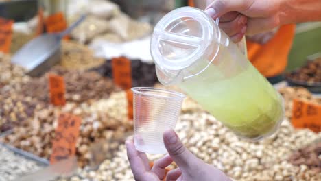 Tasting-fresh-lemonade-on-bazaar,-hand-pouring-lemonade-to-plastic-cup-close-up