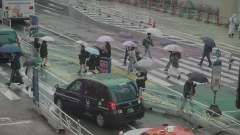 Peatones-Con-Sombrillas-En-Un-Día-Lluvioso-Cruzando-La-Calle-Con-Una-Parada-De-Taxis-En-Shibuya,-Tokio,-Japón