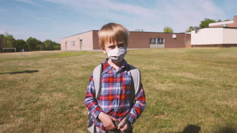 Little-boy-in-a-face-mask-turns-and-walks-toward-school