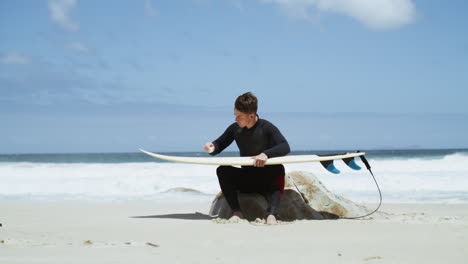 a-young-man-rubbing-wax-on-a-surfboard