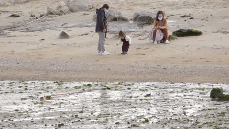 Familie-Mit-Einem-Kleinen-Mädchen,-Das-An-Einem-Sonnigen-Tag-Während-Einer-Pandemie-Am-Strand-Spielt-–-Weitwinkelaufnahme