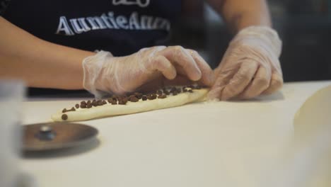 Baker's-Hands-Folding-Dough-With-Chocolate-Chips-Filling-In-A-Bakery-Kitchen,-close-up,-slow-motion