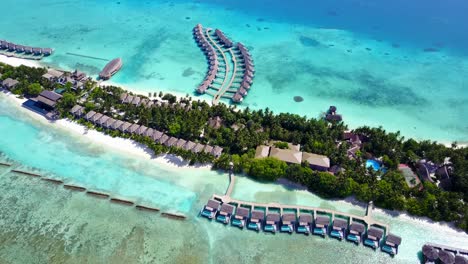 Bungalows-over-turquoise-water-of-lagoon-around-tropical-island,-connected-by-wooden-piers-with-white-sandy-beach-and-bar-restaurants-in-Bora-Bora