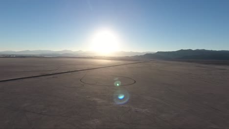 Flying-over-the-Bonneville-Salt-Flats-in-Utah-by-drone,-a-causeway-and-car-tracks-are-visible-at-sunset