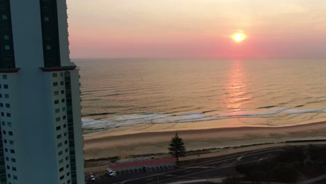Pink,-purple-sunrise-over-the-ocean-,Panning-right-with-apartments-in-foreground