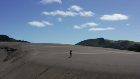Panorama-view-of-woman-standing-on-top-of-wide-sand-dune,-Bethells-Beach