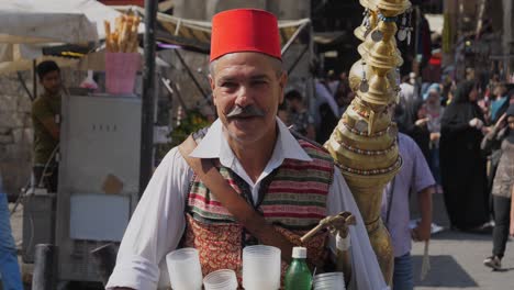 Man-selling-licorice-drink-in-a-bazaar-in-Damascus,-nods-his-head-as-a-sign-of-greeting