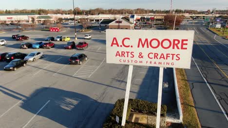 AERIAL:-AC-Moore-Arts-Crafts-Store-sign-along-highway,-shuttered,-bankrupt-company