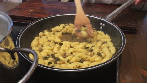 Detail-shot-of-gnocchi-pasta-in-a-pot-with-some-delicious-herbs-while-getting-cooked-and-moved-around-with-a-wooden-spoon