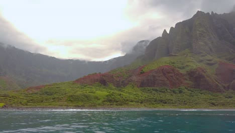 4K-Hawaii-Kauai-Boating-on-ocean-floating-right-to-left-from-waves-crashing-at-Na-Pali-Coast-State-Wilderness-Park-to-mountains-along-shoreline