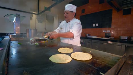 El-Chef-Mexicano-Mayor-Revuelve-Las-Verduras-En-Una-Parrilla-En-Preparación-Para-Las-Fajitas-En-Tortillas-De-Maíz