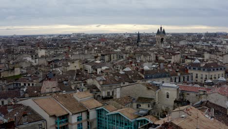 Rooftops-showing-Cailhau-City-Gate-at-the-French-city-of-Bordeaux-while-pigeon-fly-by,-Aerial-pedestal-rising-shot