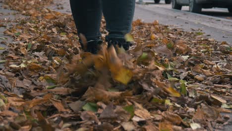 Girl-walking-and-kicking-fall-yellow-and-orange-dusty-leaves-slow-motion-front-shot