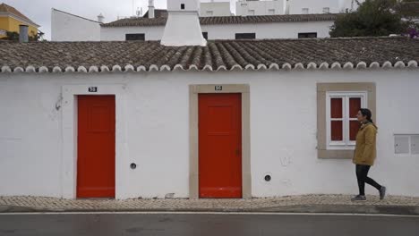 Woman-passing-in-front-of-a-traditional-house-with-red-door-in-Tavira-Algarve,-Portugal