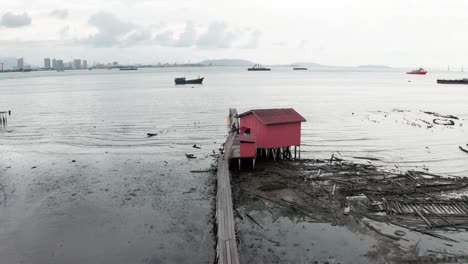Tan-Jetty-in-the-ocean-with-fishing-huts-and-boats-in-a-low-income-area-of-the-city-at-low-tide,-Aerial-drone-flyover-shot