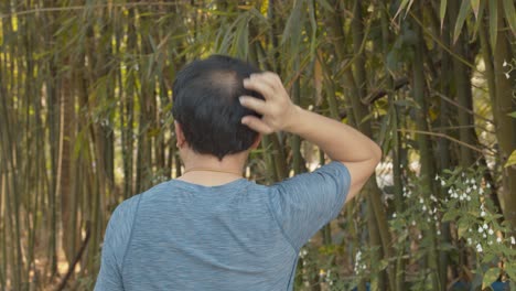 Balding-man-walking-in-a-bamboo-garden-can't-stop-scratching-his-itchy-scalp