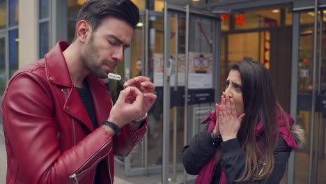 Street-magic-artist-in-red-leather-jacket-pulls-out-razor-blades-on-a-string-out-of-his-mouth-he-ate-before-in-public,-girl-with-shocked-reaction