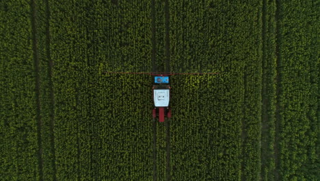 Tractor-spraying-crops-field-with-insect-repellent,-above-tracking-shot