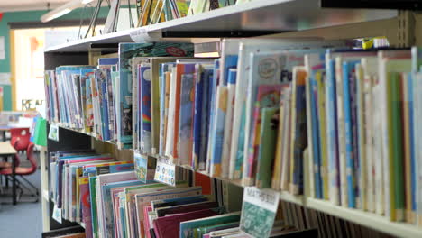 Libros-De-La-Biblioteca-Apilados-En-Estanterías-En-Una-Escuela-Primaria,-Panorámica-A-La-Derecha