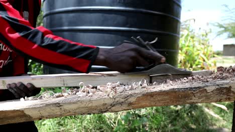 Kenianischer-Tischler-Arbeitet-Draußen-An-Einem-Projekt-Und-Verwendet-Handwerkzeuge,-Um-Ein-Brett-Für-Einen-Möbelbau-Zu-Rasieren-Und-Zu-Formen