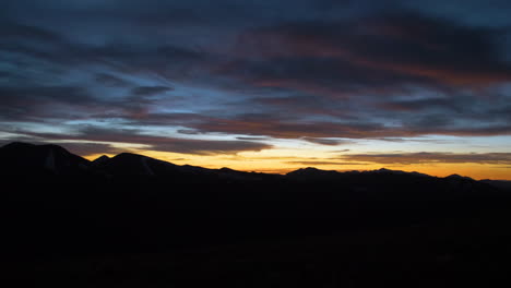 Pan-movement-looking-over-dark-mountain-range-with-colorful-sunset-sunrise-in-cloudscape
