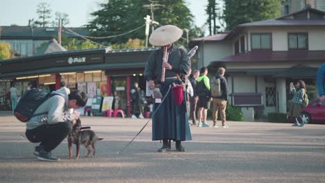 Tourist-Approach-And-Petted-The-Cute-Samurai-Dog-Standing-Next-To-Japanese-Samurai-Flute-Man-Playing-Shakuhachi-In-Maruyama-Park,-Kyoto,-Japan
