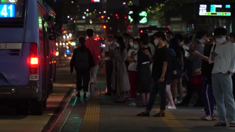 Korean-people-wearing-face-mask-stand-by-bus-stop-in-Gangnam-station,-the-downtown-city-at-night,-COVID-19,-Seoul,-South-Korea
