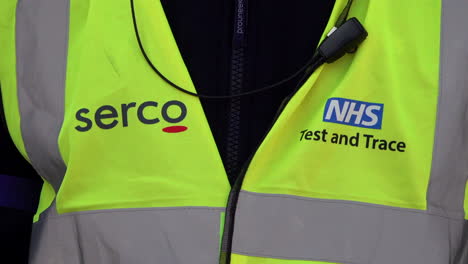 A-staff-member-at-an-appointment-only-Covid-19-testing-centre-wears-a-Serco,-NHS-Test-and-Trace-luminous-yellow-tabard