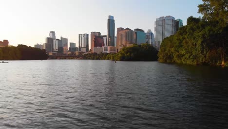 Low-drone-shot-of-a-Kayaker-paddling-towards-Downtown-Austin-Texas