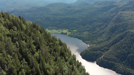 Beautiful-Norwegian-highlands,-lake-beneath-mountainside-forest,-aerial-reveal