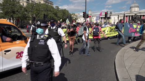 Police-in-surgical-face-masks-walk-alongside-an-Extinction-Rebellion-climate-change-protest-as-it-leaves-Trafalgar-Square-and-marches-past-traffic-waiting-at-a-red-light