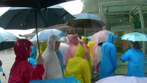 Massive-tourist-crowds-waiting-in-torrential-monsoon-rain-for-public-transport-mini-buses-at-the-foot-of-Tianmen-Mountain,-the-Zhangjiajie-National-Park,-Hunan-Province