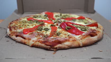Hände-Nehmen-Scheiben-Einer-Köstlichen-Pizza-Mit-Schinken,-Käse,-Roten-Paprika-Und-Oliven