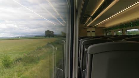 A-view-of-an-empty-UK-train-travelling-with-a-view-from-within-a-train-carriage-and-partially-the-outside-view-from-the-train-window