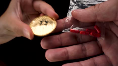 wide-angle-macro-view-of-Bitcoin-cryptocurrency-being-used-to-buy-black-market-drugs,-a-small-transparent-bag-with-red-pills-on-black-background-4k