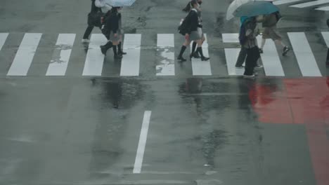 Personas-Y-Estudiantes-Caminando-Con-Una-Reflexión-Sobre-La-Carretera-Mojada-En-El-Cruce-De-Shibuya,-Tokio,-Japón,-En-Un-Día-Lluvioso