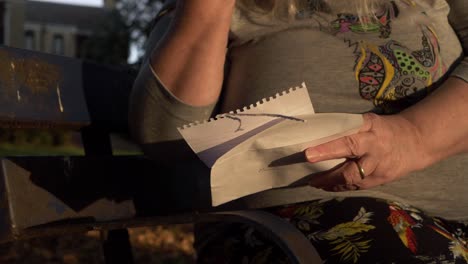 Hand-of-mature-woman-reading-letter-in-the-park-close-up-shot