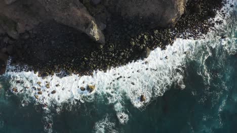 Top-down-view-of-the-beautiful-sea-waves-coming-to-the-coast-while-the-camera-is-descending-and-turning-around,-Tenerife